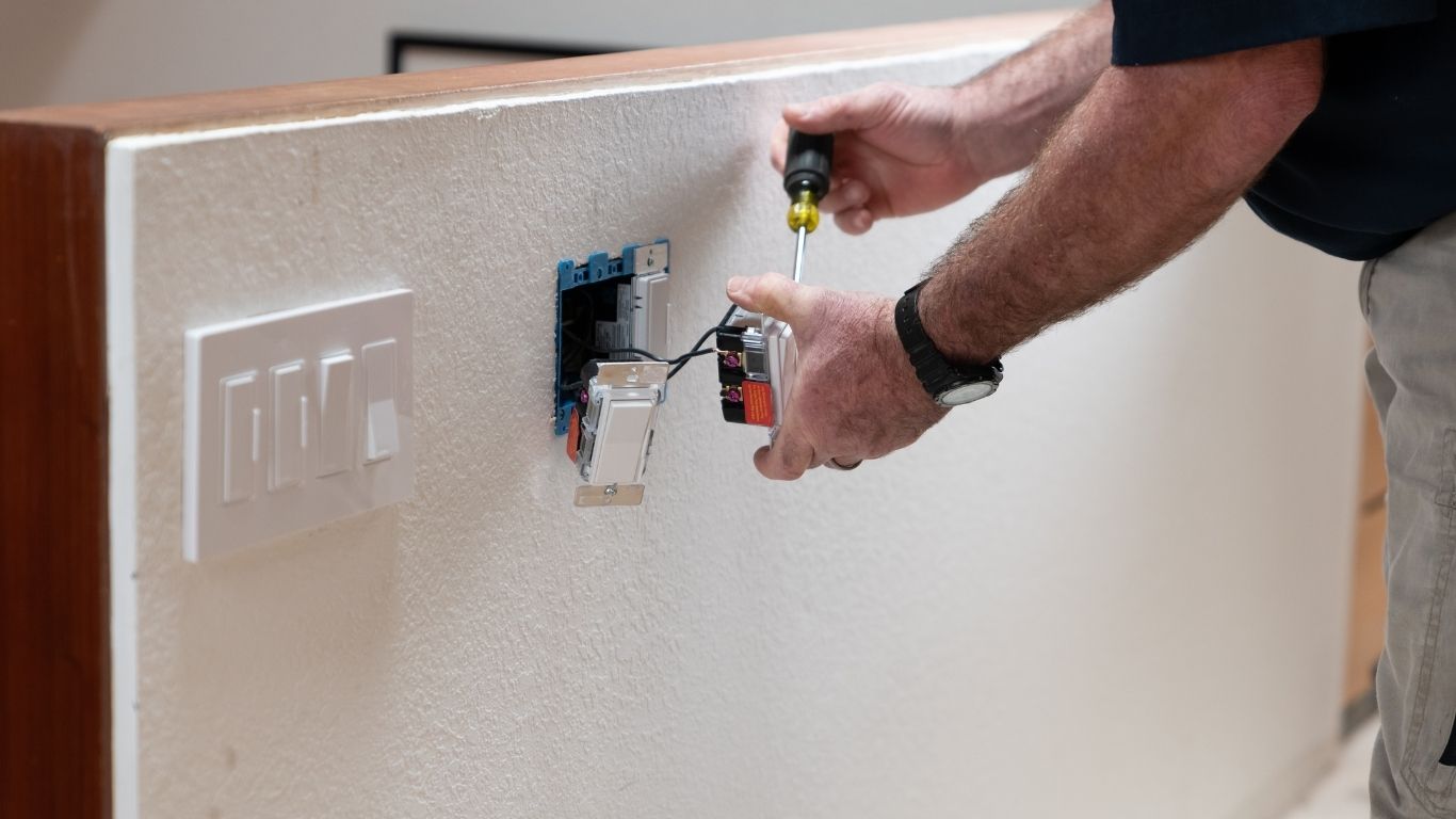 ELECTRICAL (5) A person uses a screwdriver to install or repair a light switch on a white wall.