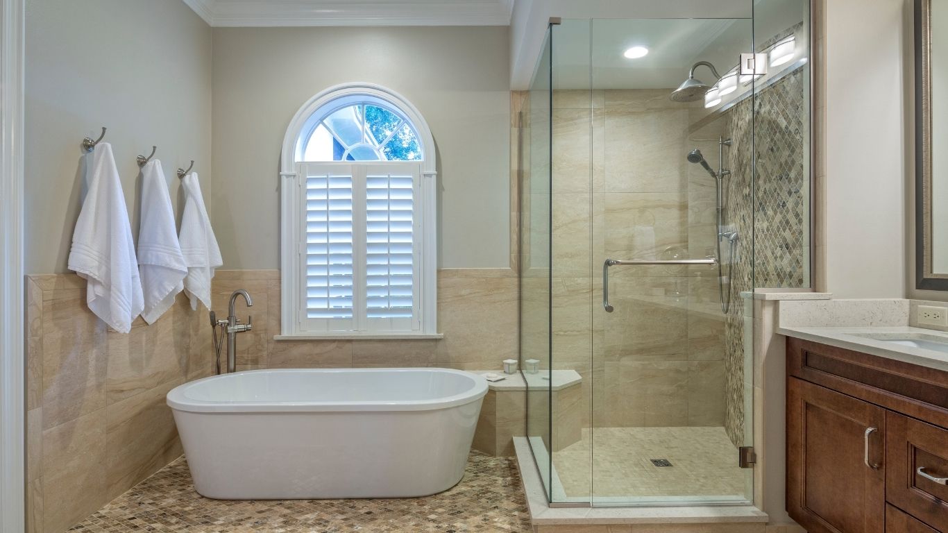 The Handyman Services Markham Modern bathroom with a freestanding bath, glass-enclosed shower, wall-mounted towels, arched window with shutters, and wooden vanity. - The Handyman Services Markham