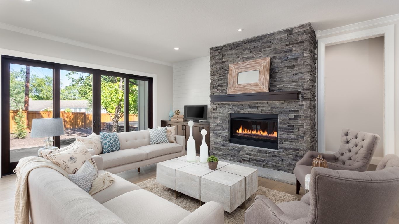 The Handyman Services Newmarket Modern living room with neutral-coloured furniture, a stone fireplace, large windows, and glass doors opening to a back garden. - The Handyman Services Newmarket