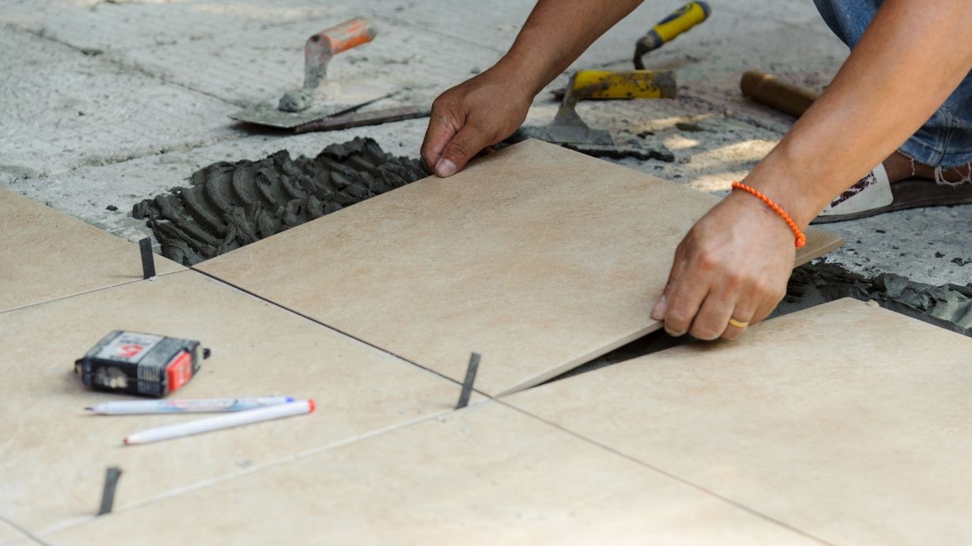 tiling (2) A person installs beige floor tiles with tools nearby, using spacers and adhesive to set the tiles evenly. - The Handyman Services York Region & Simcoe Region