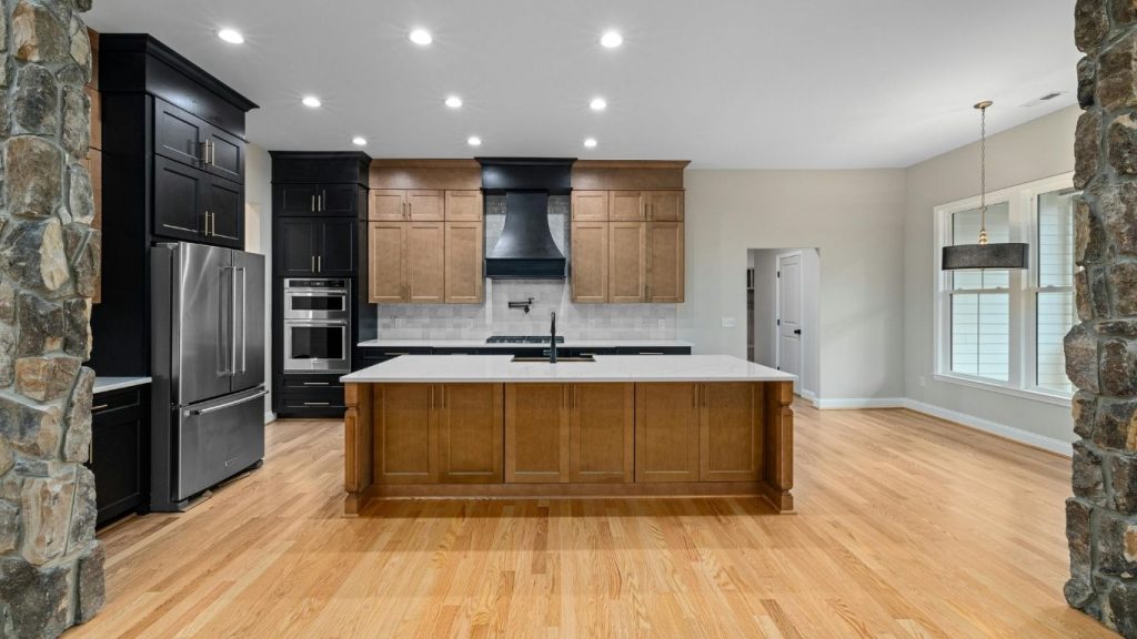Top renovation trends in Bradford this year. Modern kitchen with wooden floors, a central island, stainless steel appliances, black and wooden cupboards, and stone pillars—showcasing top renovation trends for a stylish Bradford refurbishment. - The Handyman Services York Region & Simcoe Region