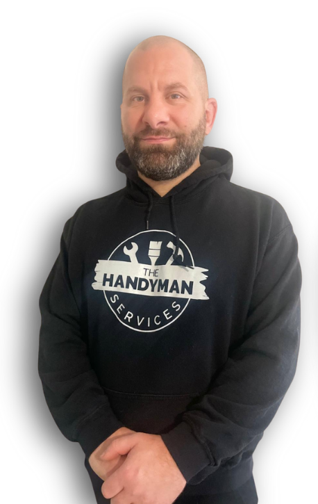 A man with a beard wearing a black "The Handyman Services" hoodie stands with his hands clasped in front of him against a plain background.