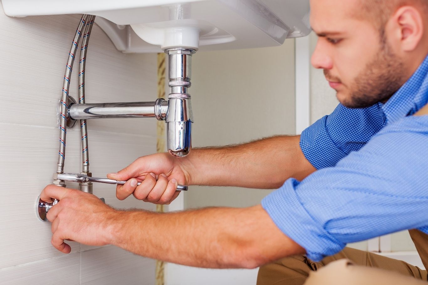 A person uses a spanner to tighten pipes under a sink, performing plumbing maintenance.