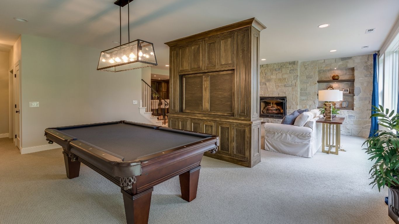 A room with a snooker table, a large wooden entertainment unit, a beige sofa, a stone fireplace, and a lamp on a side table near a window. - The Handyman Services Vaughan
