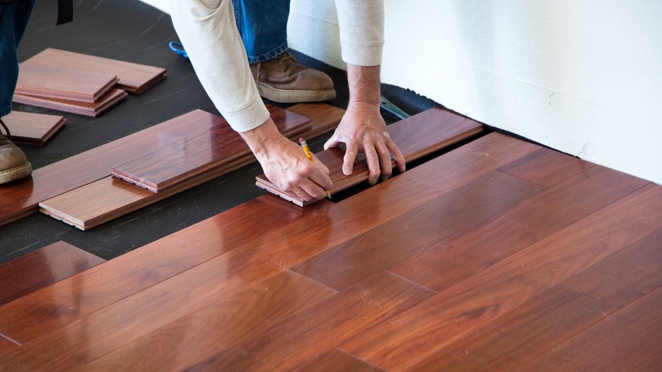 Handyman Services - Flooring - A person using a pencil to measure a wooden floor.