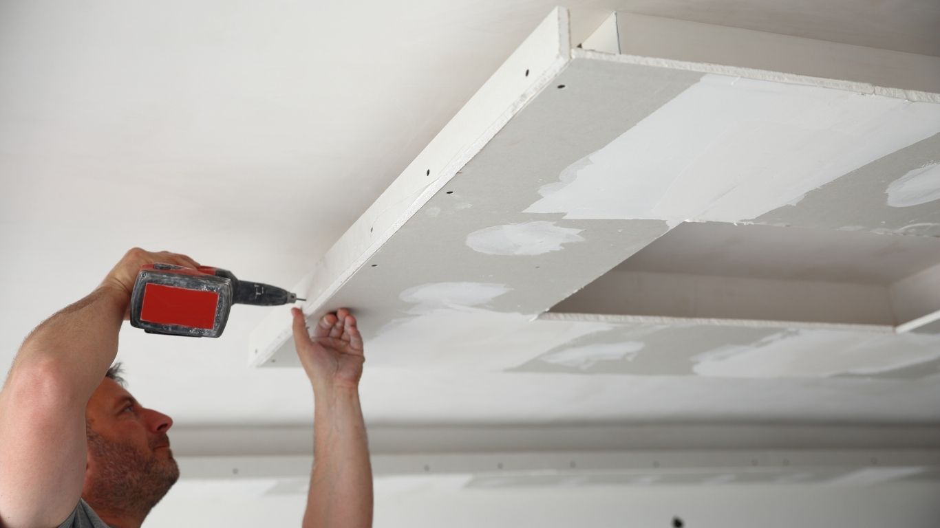 wide - drywall (7) A person uses a drill to attach plasterboard panels to a ceiling with recessed sections, with visible joint filler on the seams. - The Handyman Services York Region & Simcoe Region